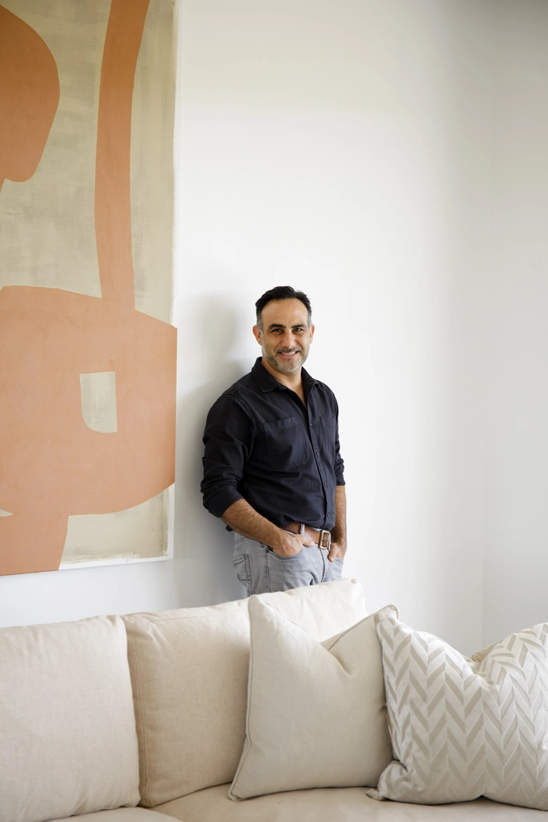 A man is standing next to a sizeable natural-coloured art piece in a modern living room.