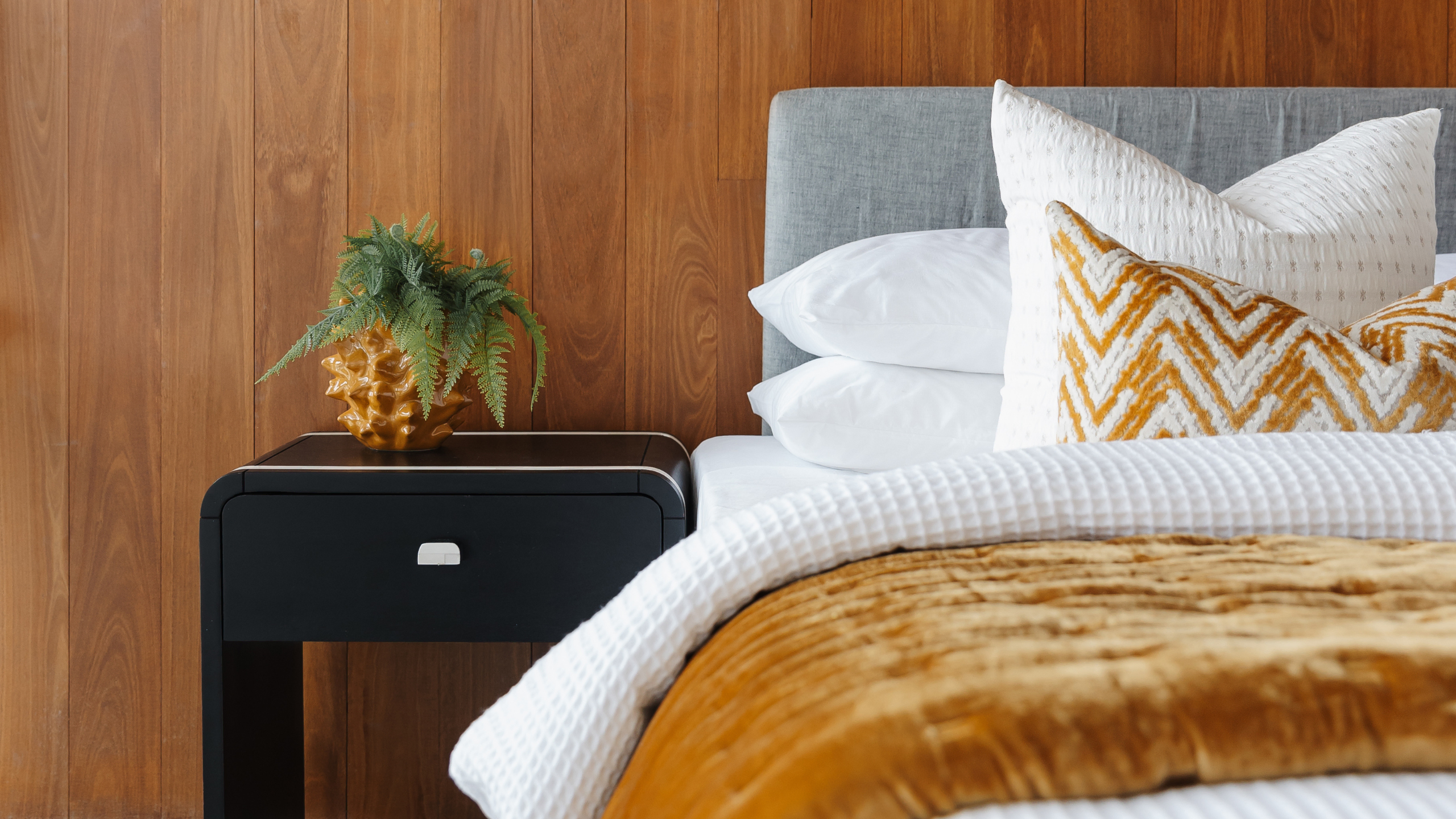 Bed and side table with grey headboard, white sheets and accents of mustard yellow