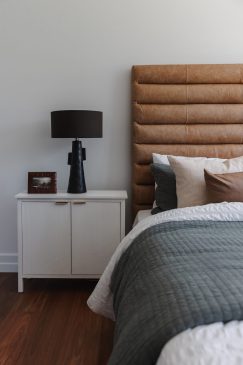 Close up of a bed with white sheets, tan coloured head board and unique lamp on the side table