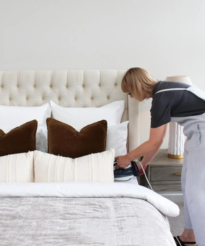 Woman ironing bed sheets on a bed